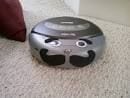 Small low-res photo of a gray robot vacuum with cartoon eyes on carpet