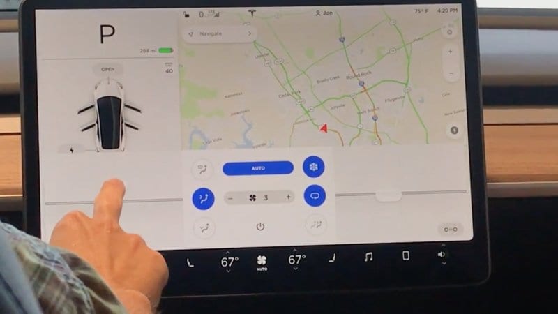 Finger tapping the Tesla Model 3 center touchscreen showing a map, car diagram and climate controls