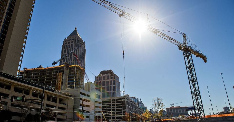 Construction cranes over Midtown Atlanta with a pointed skyscraper and the Regions building under a bright sun