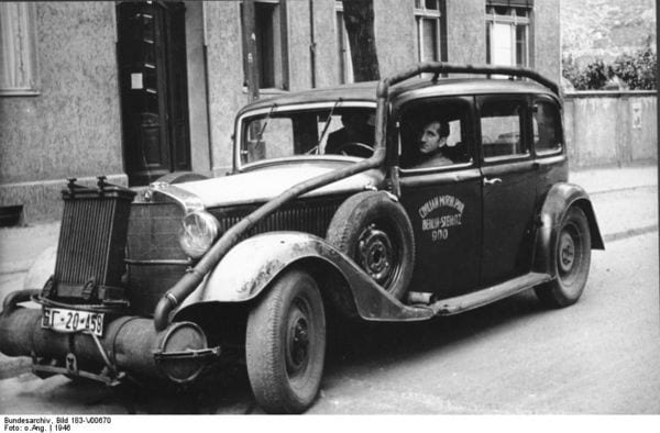 1946 black-and-white photo of a sedan fitted with a wood gas generator and pipes along its side