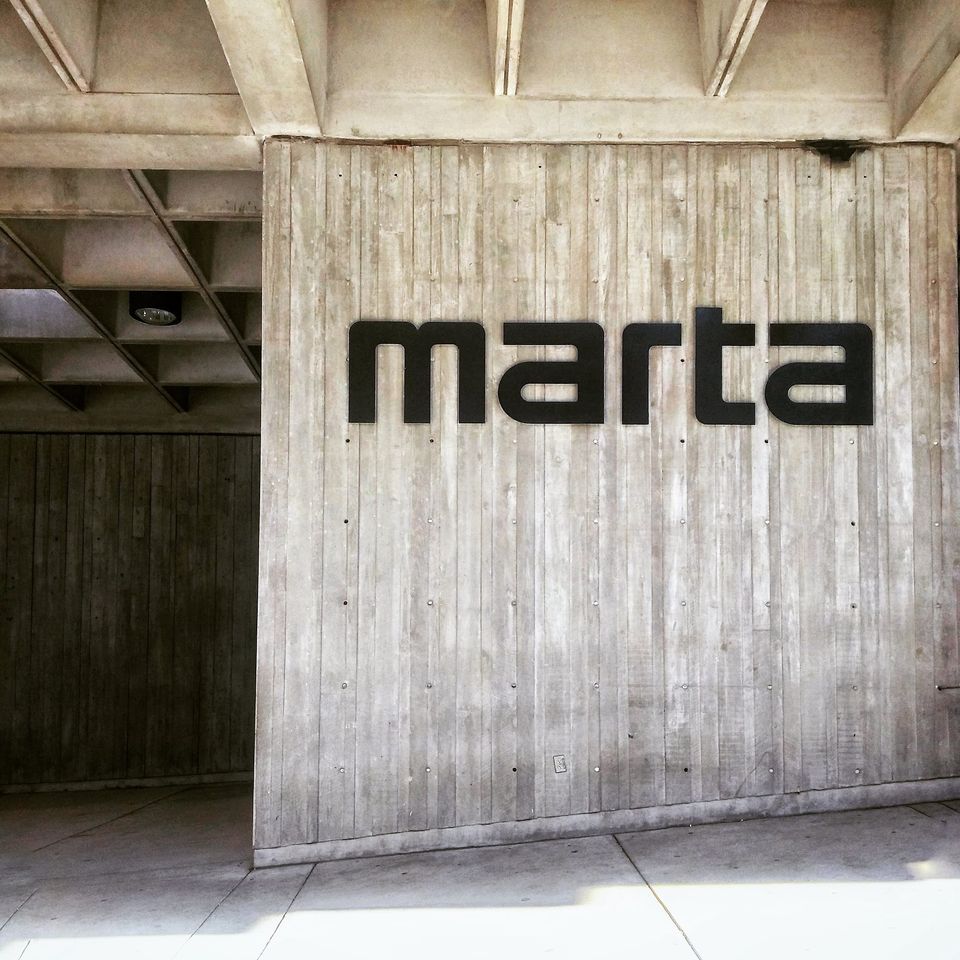 Black marta lettering on a board-formed concrete wall under a coffered ceiling