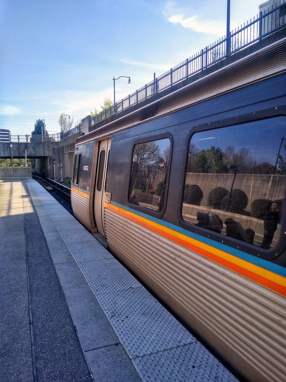 MARTA train car 115 with orange, yellow and blue stripes stopped at a sunny platform