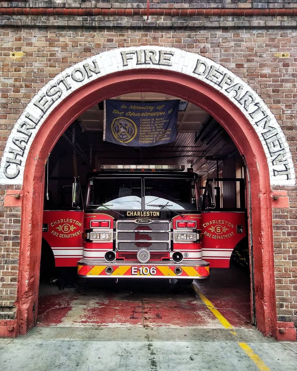 Red Charleston Fire Department engine E106 parked under a brick arch with a Charleston 9 memorial banner