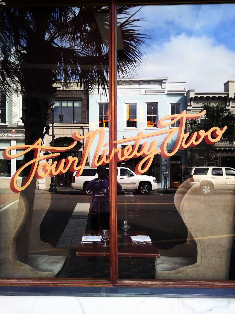 Restaurant window with Four Ninety Two in orange script reflecting palm trees and a Charleston street
