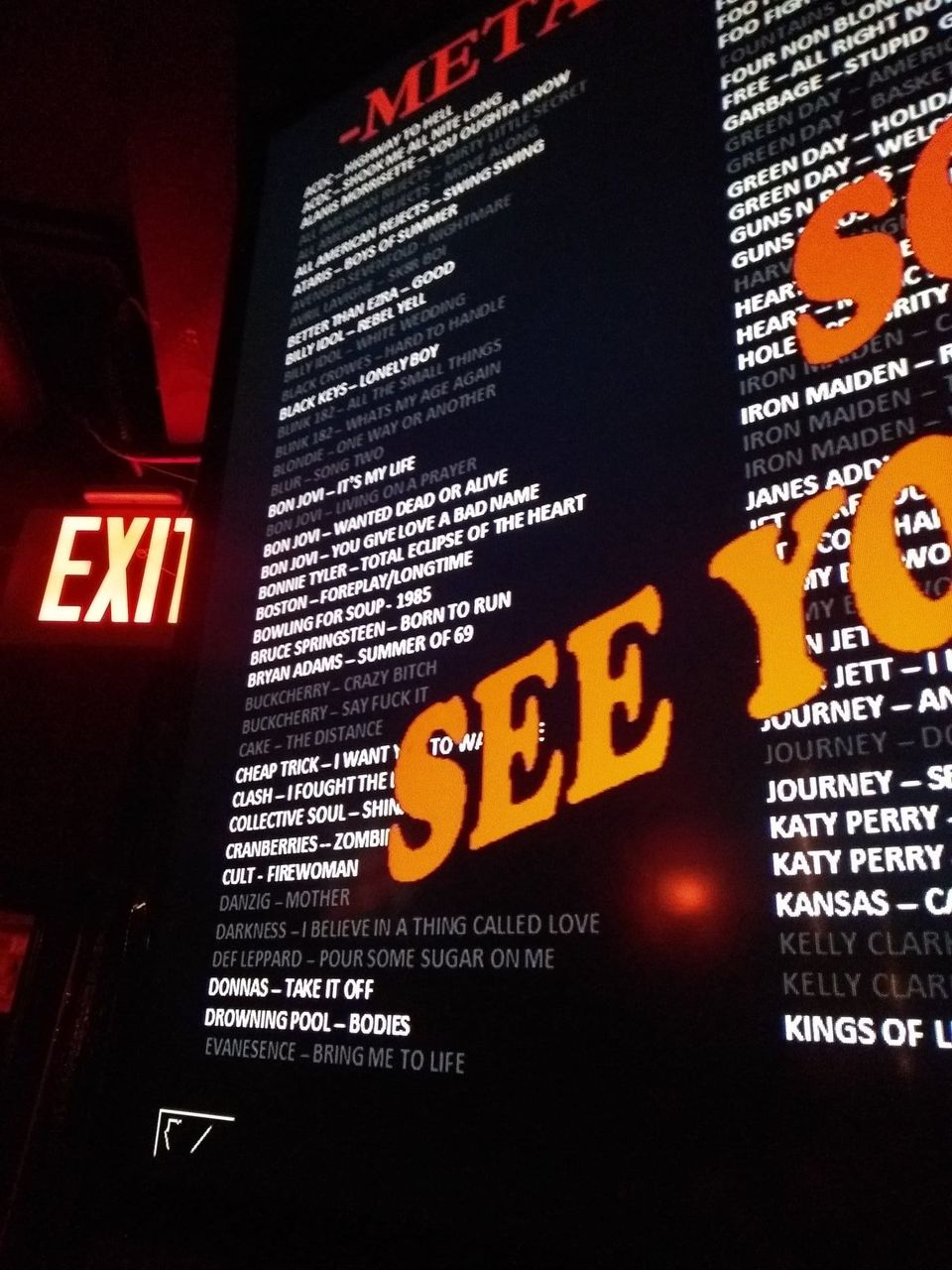 Karaoke song list from ACDC to Evanescence on a dark screen beside an exit sign with a Sold Out, See You overlay