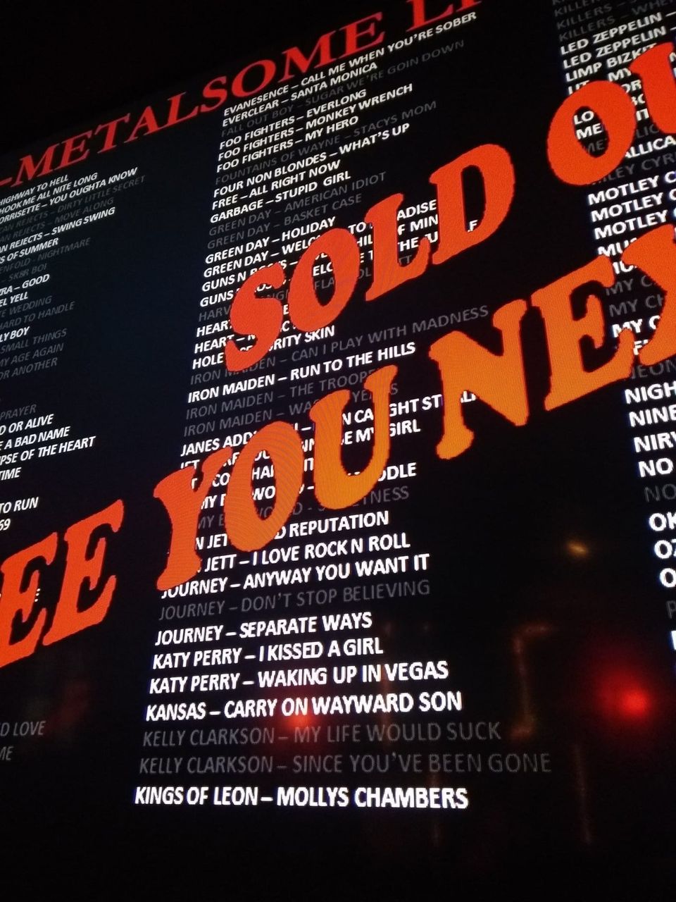 Karaoke list of songs by Foo Fighters, Green Day, Iron Maiden and Journey behind an orange Sold Out banner