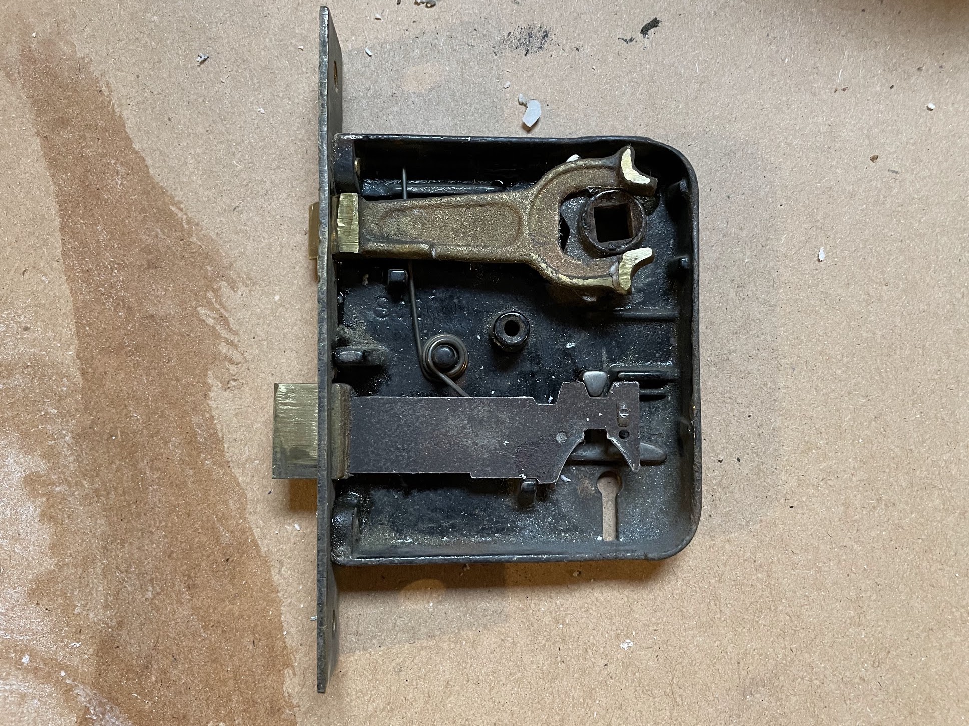 Interior mechanism of an antique mortise door lock with brass components, springs, and a bolt, viewed open on a cardboard surface