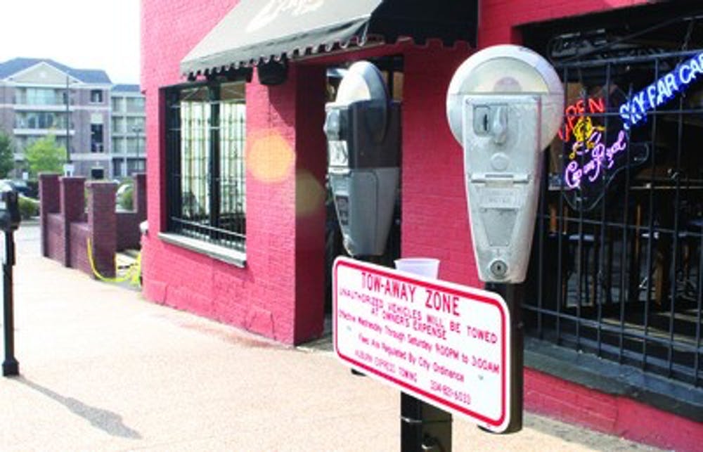 Two parking meters on a sidewalk beside a red brick building with a Tow-Away Zone sign posted below them